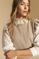 Top tejido sin mangas color negro, con cuello redondo y volados en las sisas con terminación en contraste de punto blanco. Presenta un calce recto y puño inferior acanalado con detalle de punto blanco.