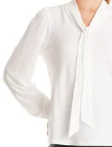 Blusa de seda fría color negro, con escote en V y lazo decorativo al cuello. Presenta mangas largas abullonadas con puños elásticos y detalles de strass aplicados en cuello, lazo y mangas.