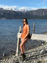 Malla enteriza color marrón con textura de relieve, escote en V con detalle de nudo frontal y aberturas laterales. Presenta bordes en color rojo contrastante.