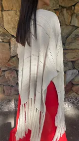Ruana de tejido de punto color crema con diseño de líneas horizontales caladas y terminación con flecos en el ruedo.