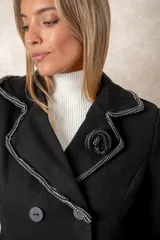 Blazer cruzado color beige, con cierre de cuatro botones frontales. Presenta detalles artesanales de encaje con perlas y cristales en la solapa y en los bolsillos delanteros.