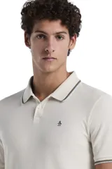 Polo de manga corta confeccionada en tejido piqué con textura tipo waffle, color beige. Presenta cuello clásico con cierre de botones y detalles de líneas en contraste en el borde del cuello y las mangas. Incluye el logo de la marca bordado en el pecho.