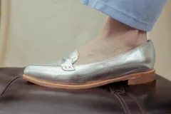 Mocasines de cuero plateado con acabado texturado, diseño clásico con costuras visibles y vira de suela natural cosida. Cuenta con taco plano de 2 cm y plantilla anatómica.