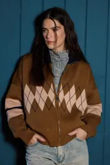 Campera tejida de punto con cierre frontal completo y cuello alto. Presenta un diseño con patrón de rombos en la parte central y franjas horizontales en las mangas.