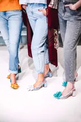 Zapato de tacón celeste con textura tejida, tira trasera y aplique de flor blanca en la punta.