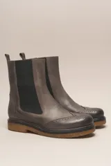 Bota tipo Chelsea de cuero vacuno color suela, con diseño brogue en la puntera y laterales. Presenta paneles elásticos laterales en color marrón oscuro, tirador trasero y suela de goma con plataforma.