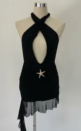 Minivestido negro con escote halter pronunciado, detalle de estrella de mar dorada en la cintura, falda drapeada y ruedo irregular con volados de tul.