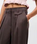Pantalón de sastrería corte recto color marrón, con pliegues frontales, cintura con trabillas y bolsillos laterales.