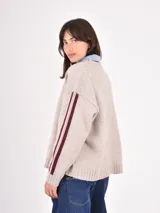 Buzo de tejido de punto en color beige, con cuello redondo, mangas largas y detalle de franjas verticales en color bordó a lo largo de los brazos.