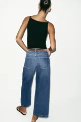 Jeans de tiro alto con pernera ancha y corte cropped. Presenta diseño de cinco bolsillos, cierre frontal con cremallera y botón, e incluye un cinturón oscuro con hebilla metálica.