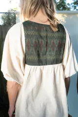 Túnica de lino color beige, de corte midi y diseño holgado, con mangas cortas y pechera combinada con tela estampada y detalles de flecos y botones.