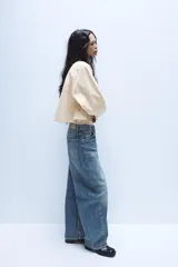 Jeans de tiro medio con diseño baggy barrel, confeccionados en denim color beige con efecto lavado. Presentan cinco bolsillos, costuras laterales torcidas y cierre frontal con cremallera y botón metálico.