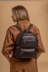 Mochila de cuero sintético con textura granulada, color negro, con compartimento principal amplio, bolsillo frontal con cierre y correas ajustables.