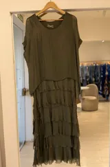 Vestido midi color verde seco, con escote redondo, mangas cortas y diseño de múltiples capas con volados y terminaciones deshilachadas.
