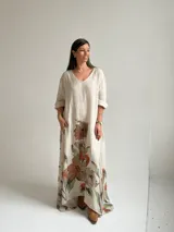 Vestido largo beige con diseño holgado, escote en V y mangas largas, adornado con un gran estampado floral en tonos marrones y verdes en la parte inferior.