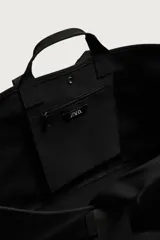Bolso shopper negro fabricado en tejido técnico, con compartimento principal con cierre de botón a presión, múltiples bolsillos exteriores frontales, doble asa de mano y asas largas de hombro.
