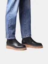 Botin de mujer de cuero negro, estilo chelsea, con elásticos laterales, tirador trasero y suela dentada de goma color caramelo.