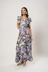 Vestido largo con estampado floral en tonos lila, verde y negro. Tiene escote en V, mangas cortas con volados y corte cruzado con lazo en la cintura.