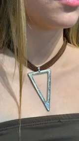 Gargantilla tipo choker con tira de gamuza marrón y dije metálico en forma de triángulo invertido.