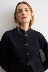 Chaqueta de jean azul oscuro, con cuello mao, cierre frontal de botones metálicos y dos bolsillos frontales de parche.