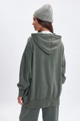 Campera deportiva de corte oversize con cierre frontal completo, capucha con cordones ajustables y puños elásticos. Presenta un acabado con efecto lavado en color verde.