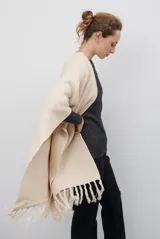 Ruana de tejido de punto en color negro, con diseño de cuello alto y terminaciones con flecos en los bordes.