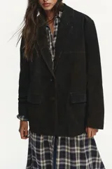 Blazer de piel de ante color marrón con efecto envejecido, solapas con muesca, cierre frontal de dos botones y bolsillos con solapa en el delantero. Cuenta con forro interior y costuras marcadas.