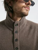 Sweater de punto color azul marino, con cuello alto, cierre frontal parcial y tapeta con botones. Presenta mangas raglán y puños y ruedo acanalados.