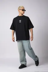 Remera de corte oversize confeccionada en algodón premium de gramaje pesado, color crudo. Presenta un bordado frontal pequeño en el centro del pecho con un diseño de dos árboles unidos por sus raíces y un parche estampado en la espalda con una silueta de mano fusionada con ramas.