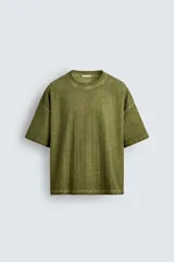 Camiseta de algodón de corte relajado (relaxed fit) con cuello redondo y manga corta. Presenta un tejido acanalado vertical (canalé) y un acabado ligeramente desgastado o lavado en tono verde oliva.