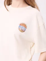 Remera de algodón con corte holgado, color crema, con estampado gráfico en la espalda que incluye un sol, montañas y mariposas con la frase Realities Rusty Collide.