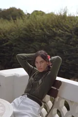 Chaqueta de punto color verde oliva con cuello redondo y manga larga. Presenta un diseño de rombos en la parte superior, cierre frontal con botones y un cinturón integrado en la cintura. Los puños y el ruedo cuentan con acabado en rib.