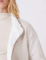 Cardigan beige con diseño de espiga, forrado en corderito sintético blanco. Presenta vivos en contraste color tostado en los bordes, cuello solapa y bolsillos tipo parche con solapa. Cierre frontal con botones carey.