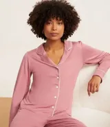 Conjunto de pijama americano largo color rosa, compuesto por camisa de manga larga con cuello solapa, abotonado delantero y pantalón con cintura elástica. Ambas prendas tienen detalles de vivos y botones contrastantes en color blanco.