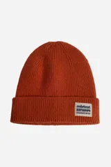 Gorro tejido de punto acanalado en color terracota, con doblez en el borde y parche rectangular con logo de la marca Mistral.