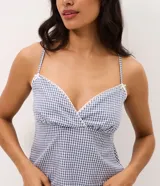 Pijama short doll de dos piezas confeccionado en algodón, con estampa de cuadros vichy en tonos azul y blanco. La musculosa presenta breteles finos, escote corazón con delicado encaje blanco y silueta fluida. El short cuenta con cintura elástica, pequeño moño frontal y terminación ondulada en el ruedo.