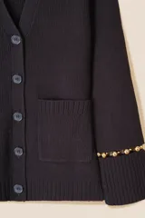 Cárdigan de punto color azul marino, con escote en V, cierre frontal con botones al tono y bolsillos de parche. Presenta mangas largas con aberturas decoradas con cuentas doradas en los puños.
