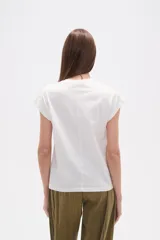 Remera blanca de algodón con mangas cortas y cuello redondo. Presenta un bordado floral en tonos rosados y rojizos en la zona del hombro derecho.