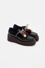 Zapato tipo mocasín de plataforma color bordó, confeccionado en una combinación de cuero liso y gamuza. Presenta cordones bicolores con detalle de borlas decorativas en el empeine.