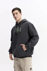 Canguro con capucha y cordones ajustables, confeccionado en algodón con detalle de estampado frontal en tonos verdes. Presenta un bolsillo tipo canguro delantero, puños y ruedo acanalados.