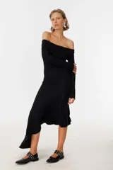 Vestido midi negro con escote off-shoulder, mangas largas y falda con volados asimétricos.