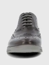 Zapato tipo Oxford estilo brogue con detalles perforados en la puntera y laterales. Presenta capellada de cuero en tono marrón oscuro, cordones al tono y suela de goma gris con diseño deportivo.