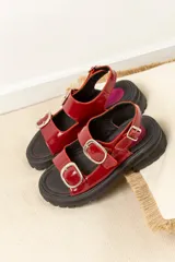 Sandalias de plataforma estilo chunky en color negro, confeccionadas en material sintético efecto charol. Presentan dos tiras ajustables con hebillas metálicas plateadas y una tira trasera con hebilla para mayor sujeción. Suela dentada de goma.