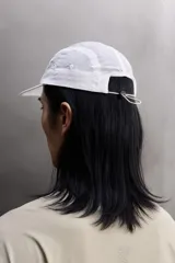 Gorra blanca confeccionada en tejido técnico ligero con estructura ripstop, resistente a desgarros. Cuenta con ajuste elástico en la parte posterior y estampado frontal de logo con relieve.