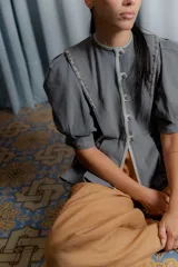 Chaqueta gris de silueta femenina con mangas abullonadas, cuello redondo y cierre frontal con botones forrados. Presenta detalles de bordado artesanal a mano en los hombros y solapas.