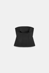 Top negro de tejido satinado, sin tirantes y con escote recto. Presenta costuras marcadas y diseño con peplum en la parte inferior, con cierre de cremallera oculta en la espalda.
