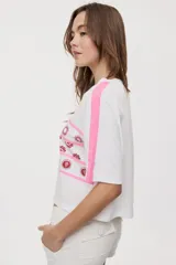 Remera blanca de manga corta, con cuello redondo, calce relajado y estampado frontal con motivos gráficos de soles y símbolos marinos en tonos rosados y bordo, además de líneas horizontales.