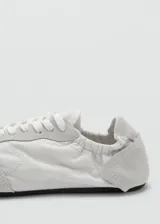 Sneaker Sofi de estilo minimalista en color gris claro, confeccionada en una combinación de piel vacuna y poliéster con detalles de gamuza en la puntera y el talón. Presenta cierre con cordones y un diseño fruncido en la parte trasera con elástico.