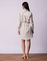 Vestido camisero corto a rayas verticales celestes y blancas, con cuello con solapa, abertura frontal con botones, dos bolsillos de parche en el pecho y lazo de ajuste en la cintura.