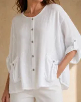 Blusa de lino color blanco con cuello redondo, cierre frontal con botones, bolsillos aplicados y detalles de bordado inglés.